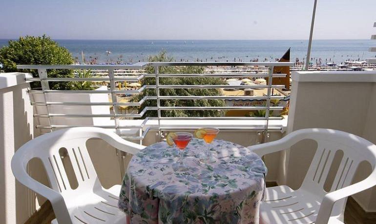 Terrazza con vista mare, tavolo e sedie bianche.