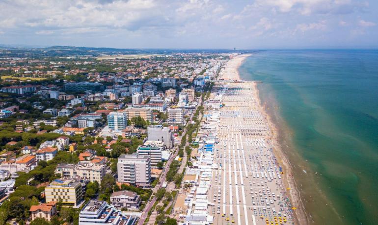 Spiaggia affollata con ombrelloni e mare azzurro, città sullo sfondo.