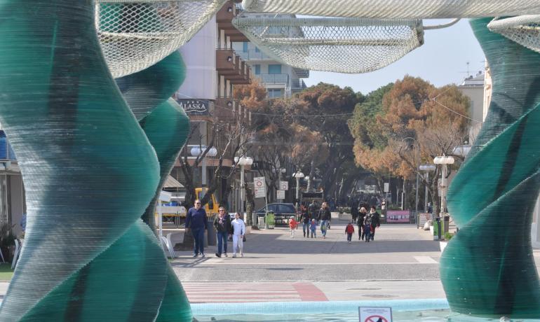 Strada pedonale con sculture verdi e persone che passeggiano.