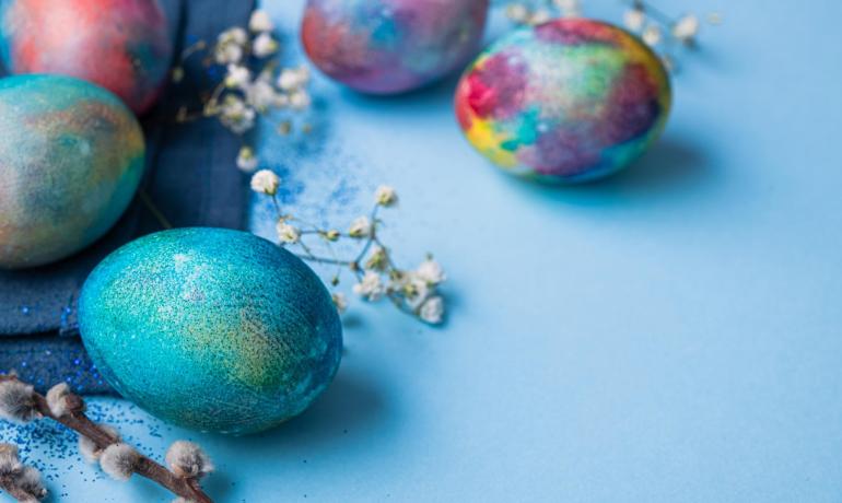 Uova colorate con fiori e rami su sfondo blu.