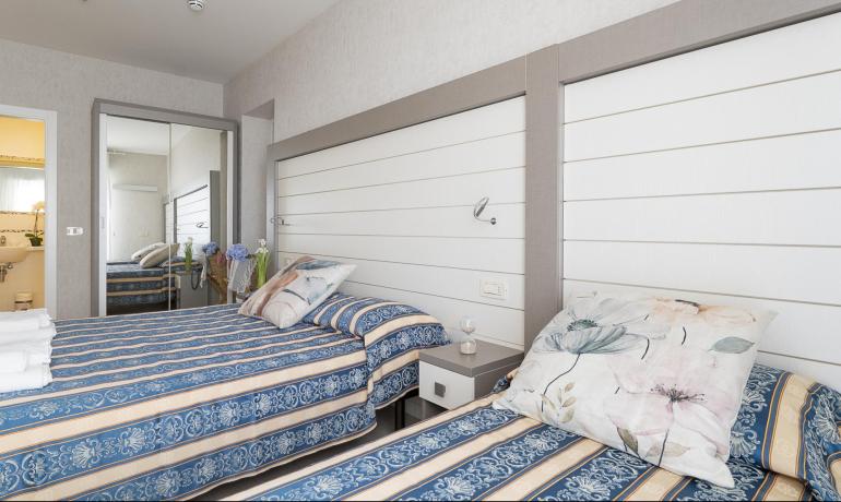 Bright room with twin beds, blue patterned covers, and flowers on the nightstand.