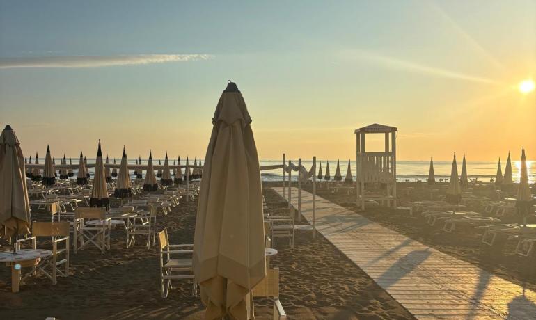 Empty beach at sunrise, closed umbrellas, serene and bright atmosphere.