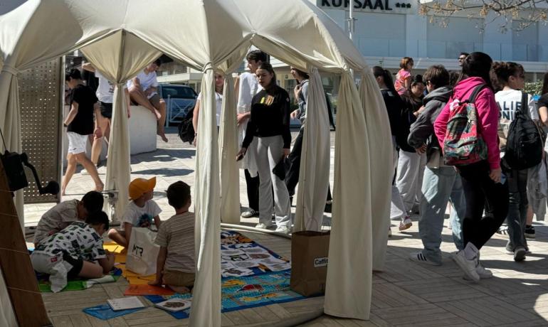 Children play under a gazebo, while youths chat outdoors.