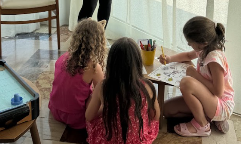 Bambini colorano felici sotto lo sguardo attento di un'educatrice sorridente.